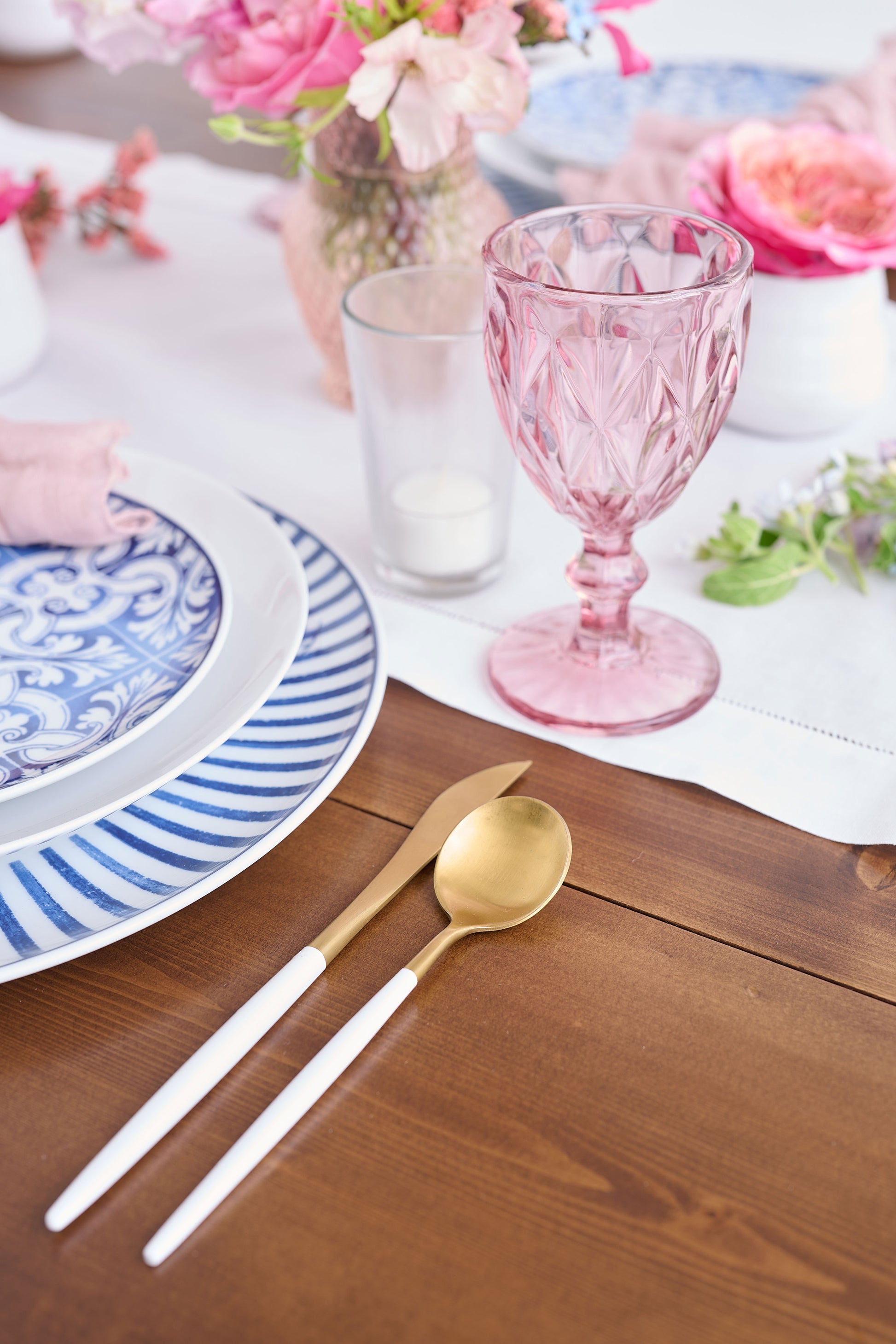 Tabletop setting with blue and white pattern dishes with pink florals, pink waterglass, and gold hardware.