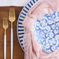 Gold utensils with pink napkin and blue and white dishes.