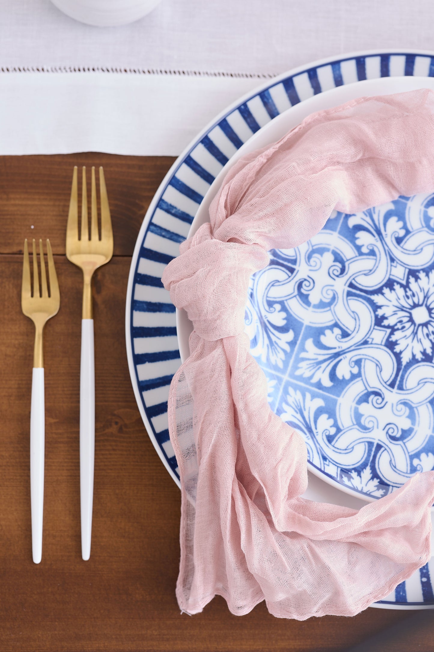 Gold utensils with pink napkin and blue and white dishes.